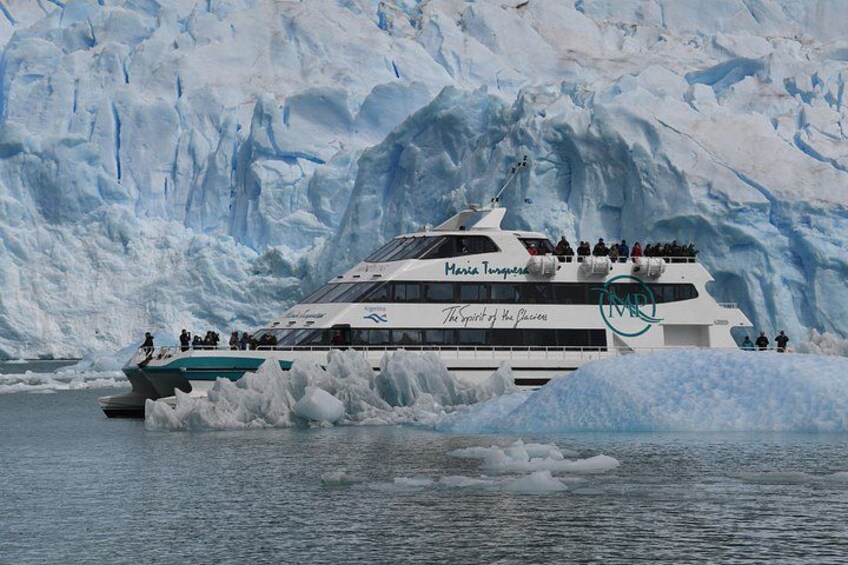 Un crucero llamado 'Marie Tournier' con pasajeros en la cubierta, rodeado de icebergs y un glaciar al fondo. 1