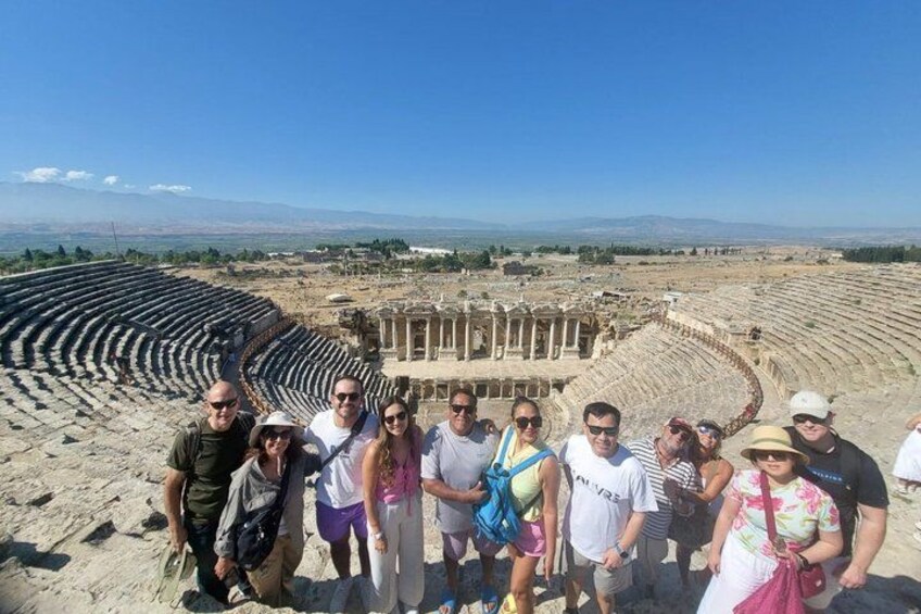 A group of people standing in front of an ancient amphitheater with stone seating and columns. 2