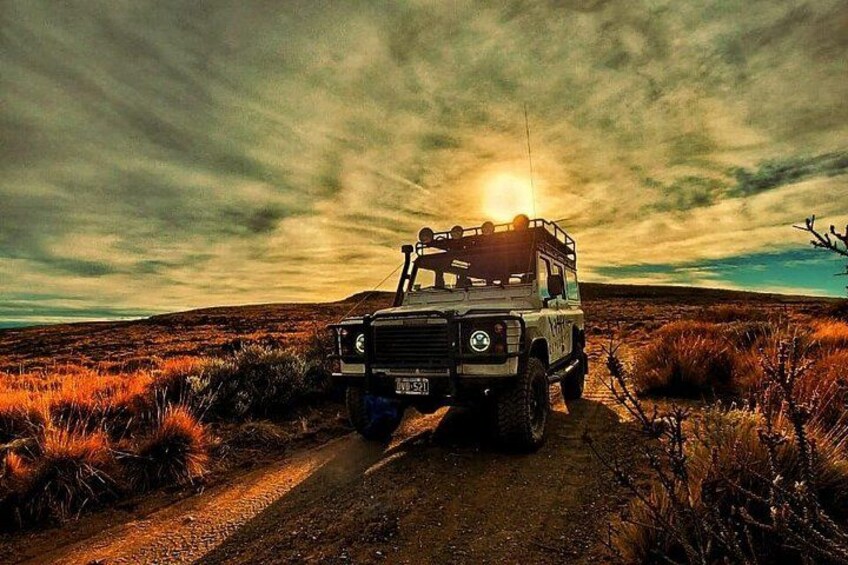 A vehicle on a dirt road with a sunset in the background. 5