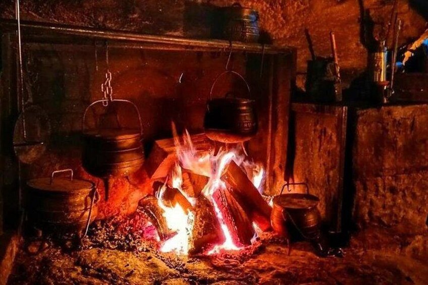 A traditional fireplace with burning logs, a hanging pot, and a metal container. 4