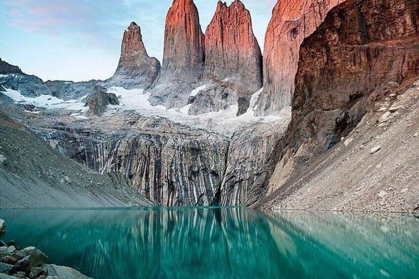 A mountainous landscape with a turquoise lake reflecting the peaks, a snow-covered ridge, and a clear sky. 1