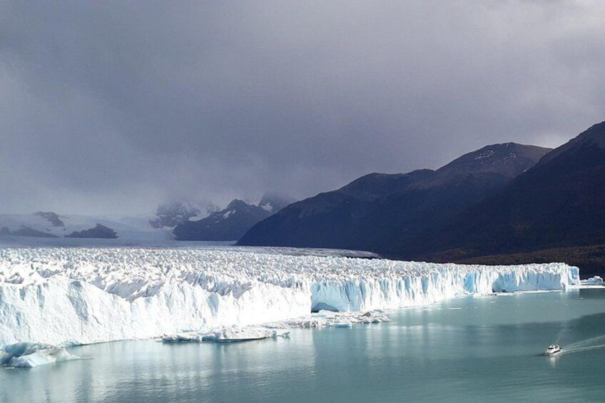 A glacier calving into a calm body of water with mountains in the background. 2