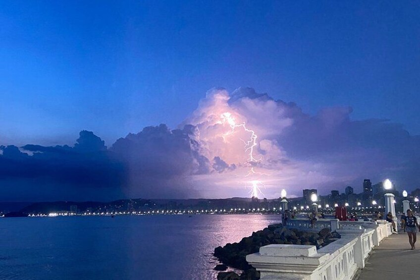A waterfront cityscape with a lightning storm in the distance. 1