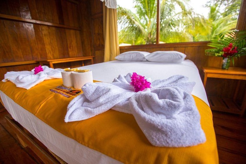 A wooden room with a bed, towels, and a vase with flowers. 3