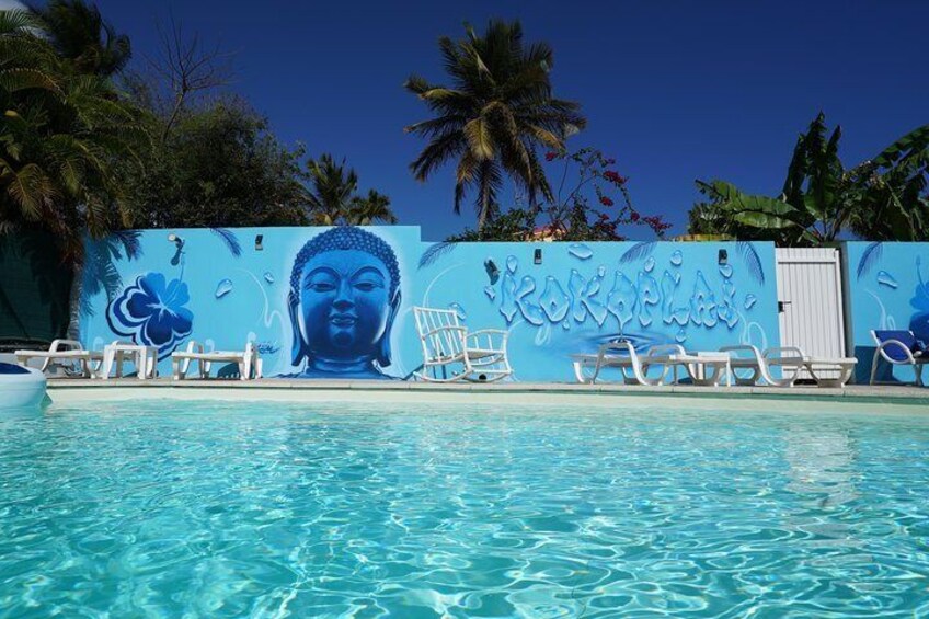 Ein Swimmingpool mit einem Wandgemälde eines Buddha und tropischer Blumen. 4