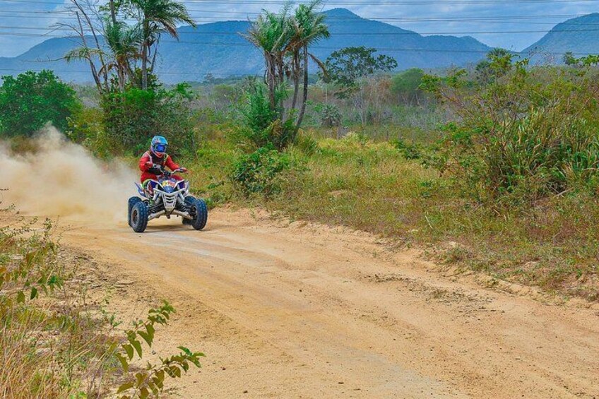 Une personne conduit un quad sur un chemin de terre, entourée de verdure et de collines. 4