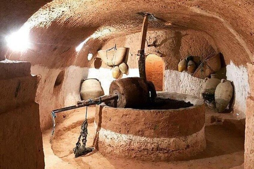 An underground stone structure with a central water well, stone walls, and various pottery and tools. 5