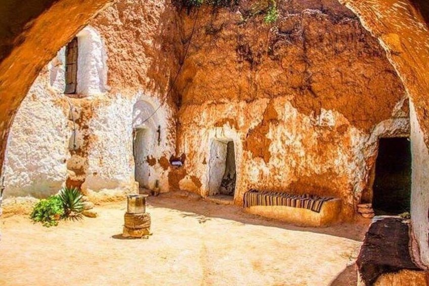 An ancient cave with stone walls, a bench, and a small table. 2