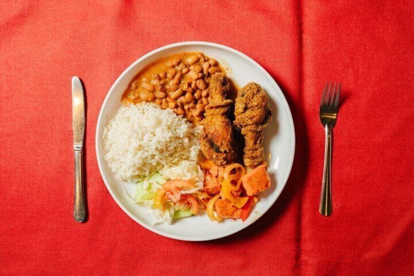 A plate of food with rice, beans, meat, and vegetables on a red tablecloth. 2