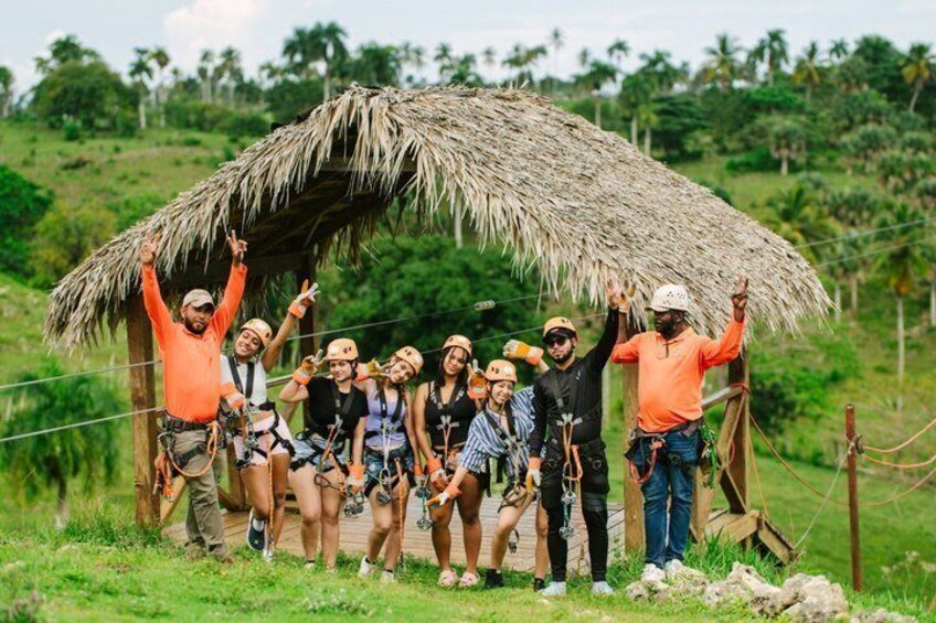 A group of people posing under a thatched structure in a tropical setting. 5