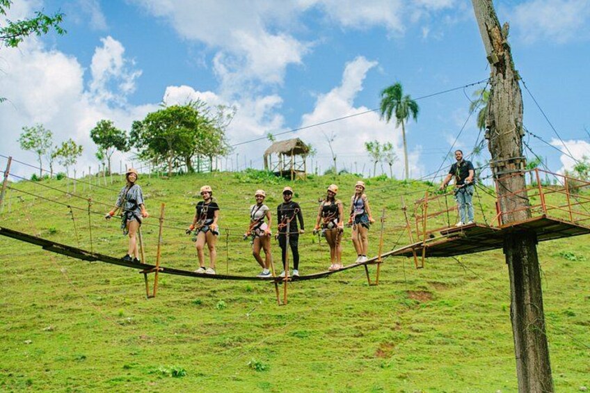 People on a rope bridge in a grassy area with trees and a clear sky. 5
