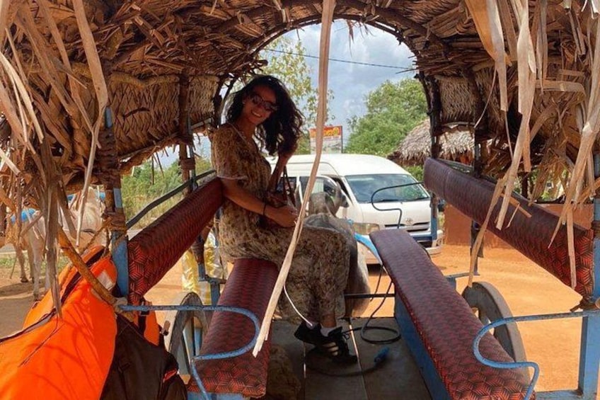 A person sitting under a thatched roof structure with a vehicle in the background. 3
