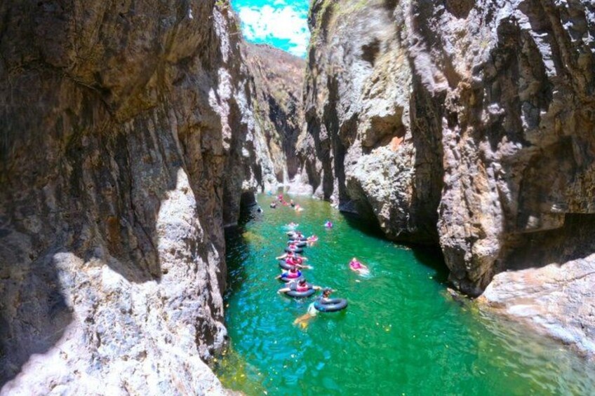 A narrow canyon with clear turquoise water, kayaks, and a person in a wetsuit. 1