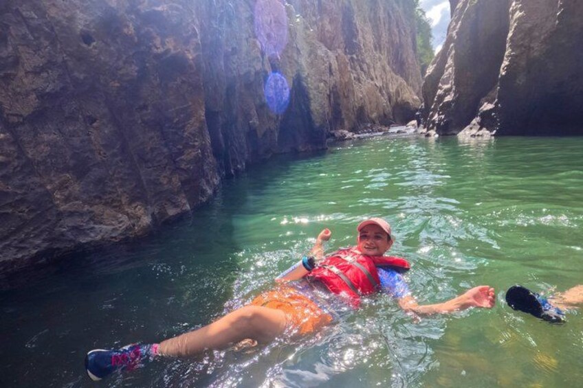 A person floating in a narrow canyon with steep rock walls and clear water. 5