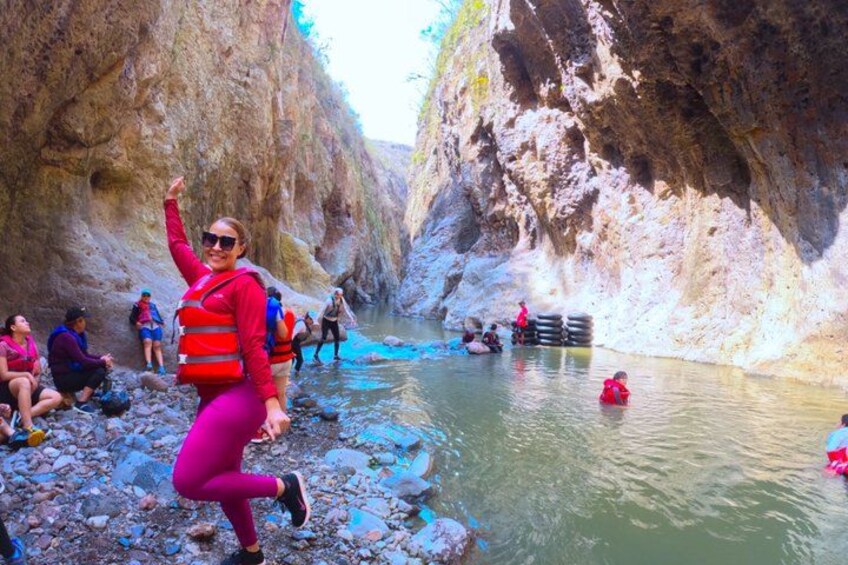 A group of people in a canyon with a river, some wearing life jackets and others standing on rocks. 3