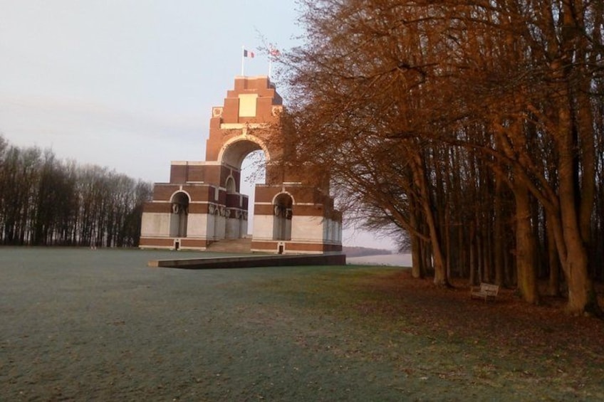 A large stone monument with an archway, surrounded by a grassy field and trees. 2