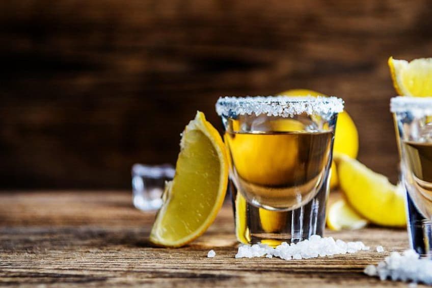 Due bicchierini con liquido giallo, circondati da fette di limone e sale. 3