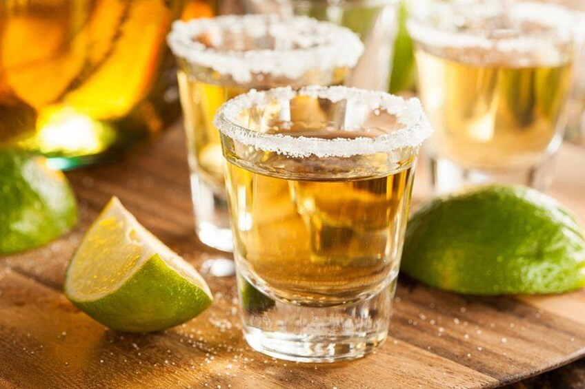 Bicchierini con un liquido dorato e spicchi di lime su un tavolo di legno. 1