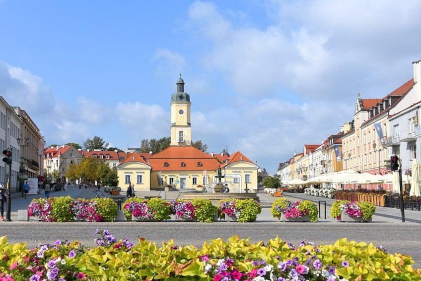 A town square with a prominent clock tower, surrounded by colorful flower beds and historic buildings. 5