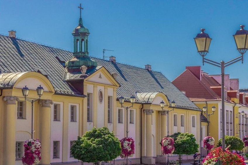A street with yellow buildings, a green dome, and flower-lined sidewalks. 2