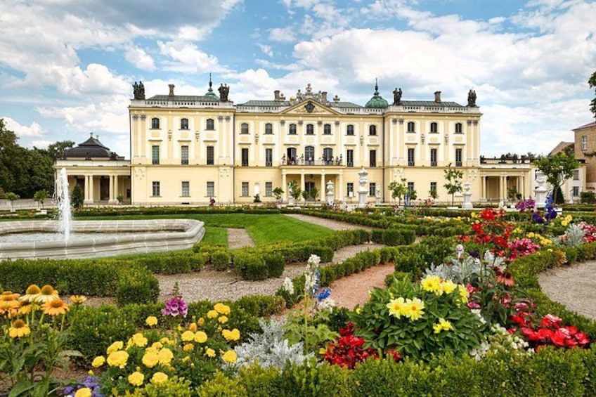 A large classical building with a formal garden in front, including a fountain and colorful flower beds. 3