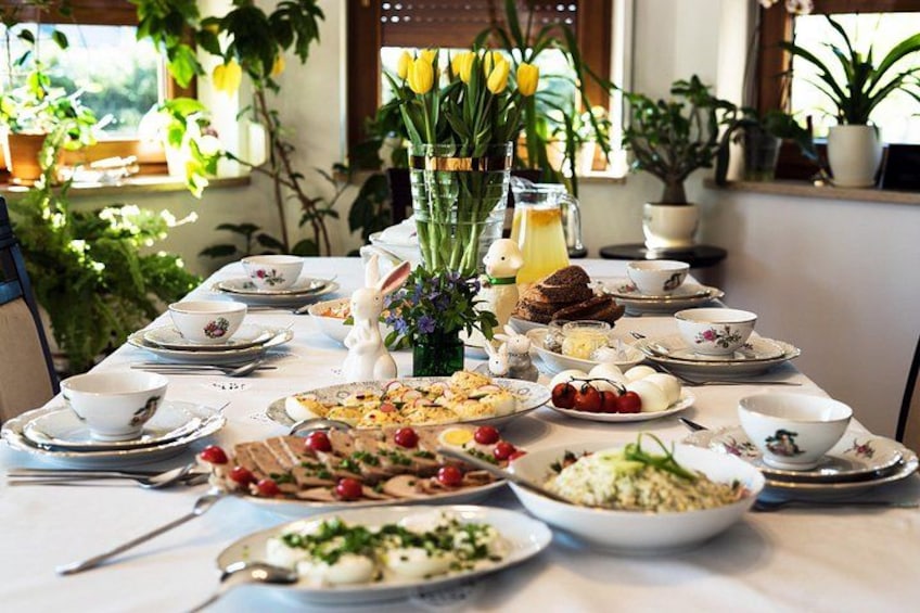 A table set for a meal with various dishes, a vase of flowers, and a window with plants. 3
