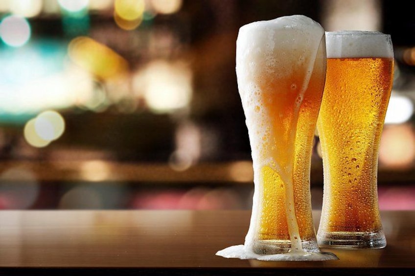 Two tall glasses of beer with foam on a bar counter. 1