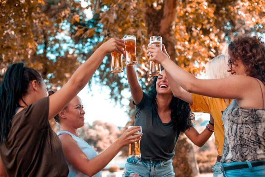 A group of people toasting with beer glasses outdoors. 2