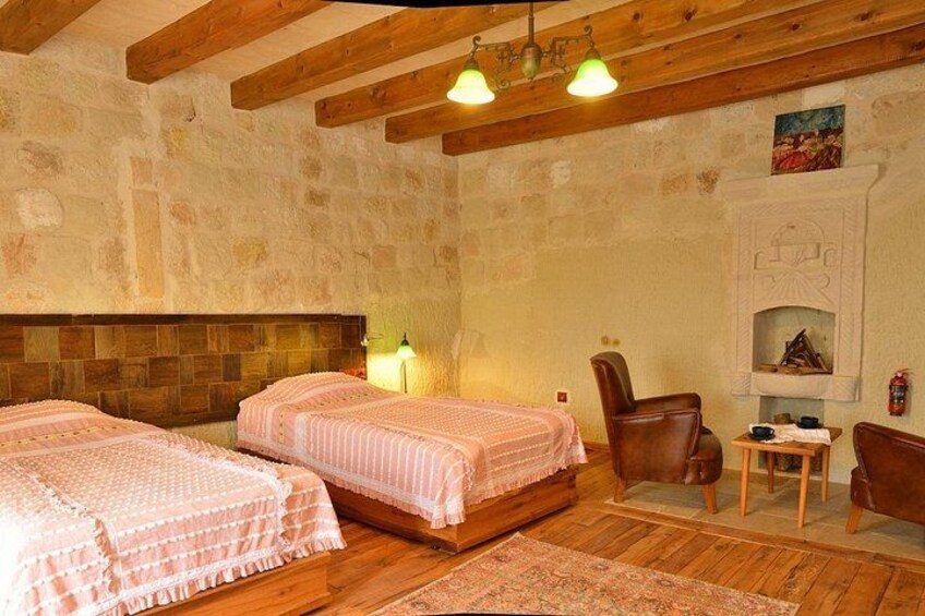 A cozy room with wooden floors, two beds with pink bedding, a fireplace, and a stone wall. 2