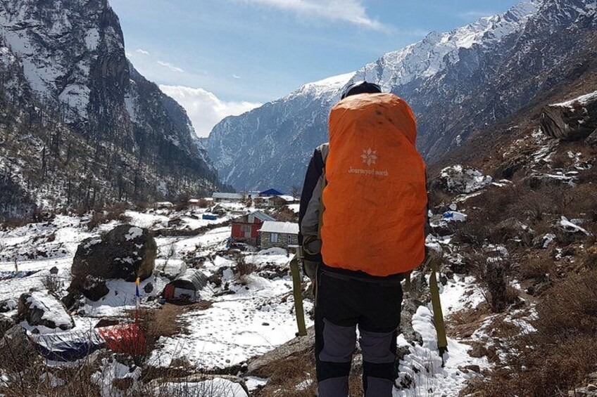 A person in an orange vest standing on a snow-covered mountain with a view of a valley and a building. 4