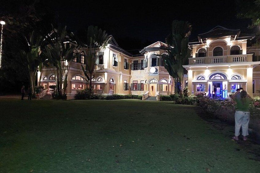 Una grande villa illuminata di notte, con un prato curato e piante tropicali. 2