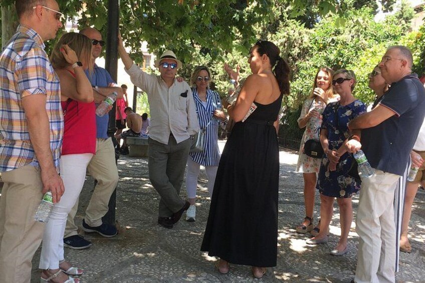 A group of people gathered outdoors, some standing and others walking, under trees. 3