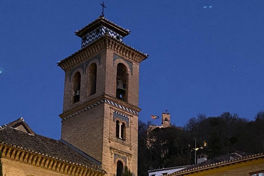 A brick tower with a clock and bell, surrounded by buildings and trees. 5