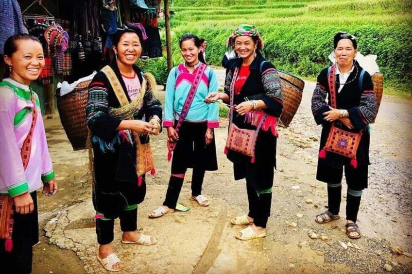 A group of people in traditional attire standing on a dirt path with a green field in the background. 2