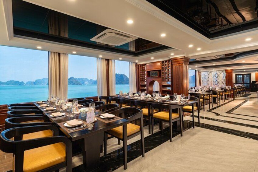 A restaurant with a long table set for dining, large windows with a view of the sea, and a modern interior design. 2
