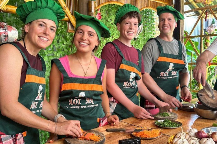 Vier mensen met groene hoeden en schorten bereiden eten aan een tafel met groenten en kookgerei. 4