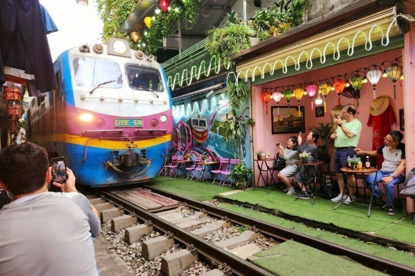 A colorful train on tracks, a small outdoor cafe with patrons, and a decorative wall. 3