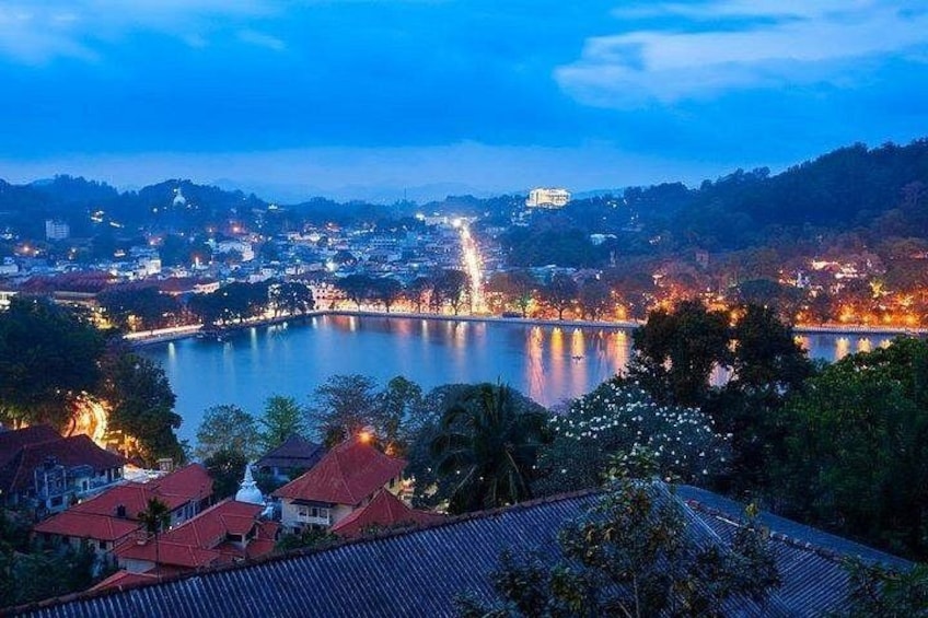 A cityscape at dusk with a river, buildings, and a hill in the background. 1