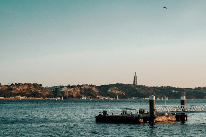 A calm body of water with a lighthouse in the distance, a dock with a boat, and a bird flying overhead. 2