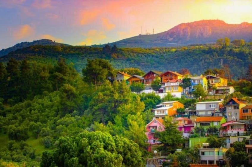 Un village perché sur une colline, avec des maisons aux couleurs vives, une végétation luxuriante et une montagne en arrière-plan. 2