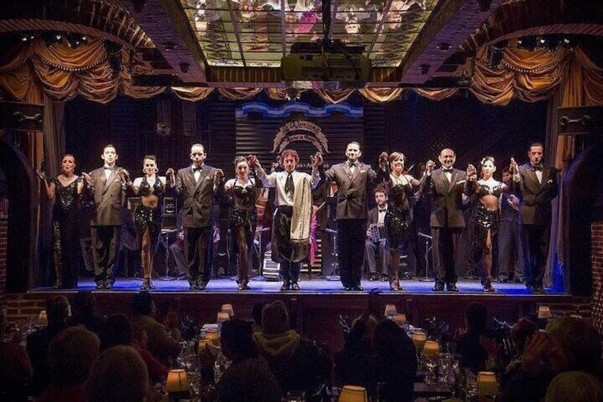 A group of people on a stage with a chandelier, audience, and a sign that reads 'GREAT'. 2