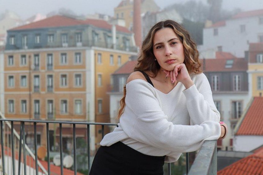 A person leaning on a balcony railing with buildings in the background. 2