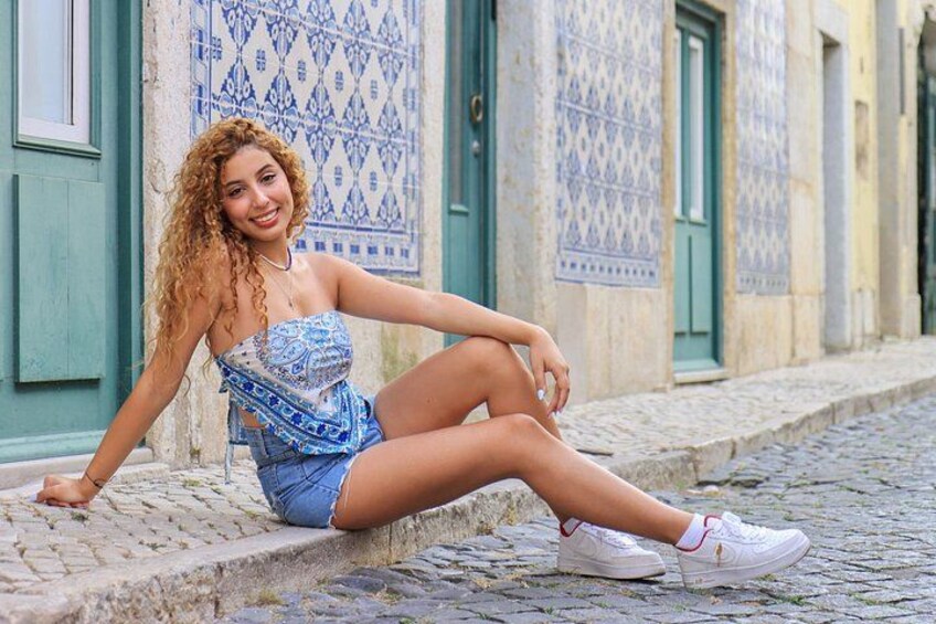 A person sitting on a cobblestone street with patterned tiles on the buildings in the background. 3