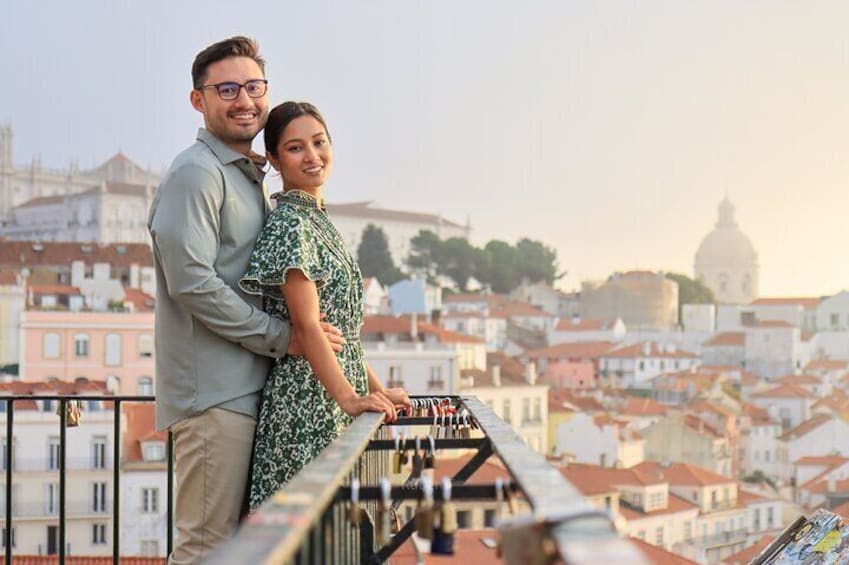 A couple standing on a balcony overlooking a cityscape with historic buildings and a dome in the background. 1