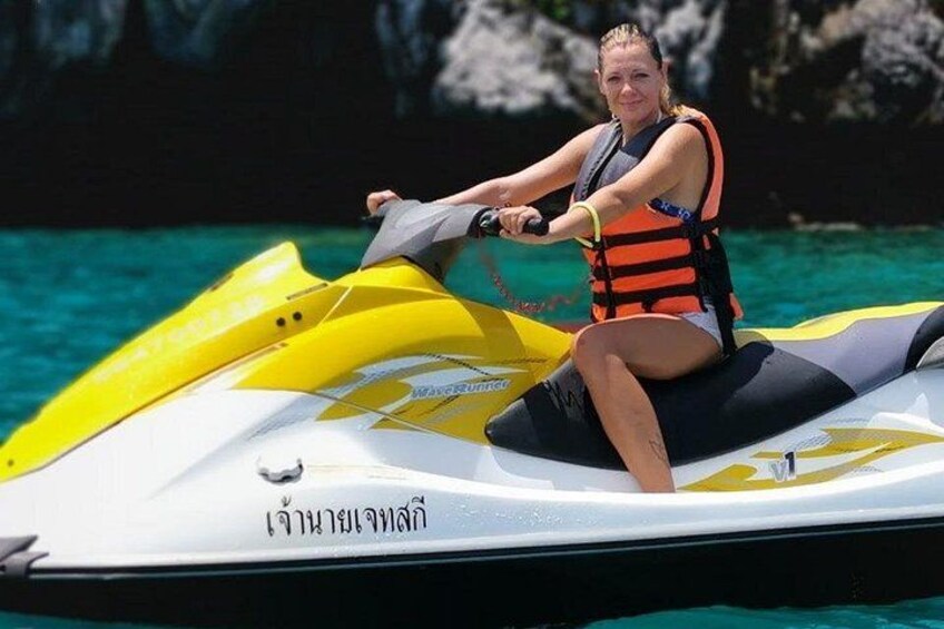 En person kører på en jetski på vandet med klart, blåt vand og klippeformationer i baggrunden. 5