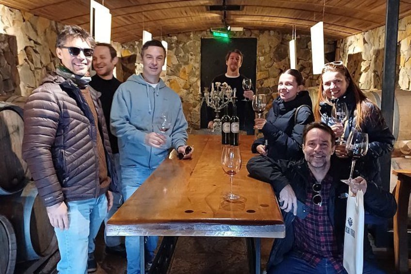 A group of people at a wine tasting event in a rustic cellar with wooden barrels and stone walls. 2