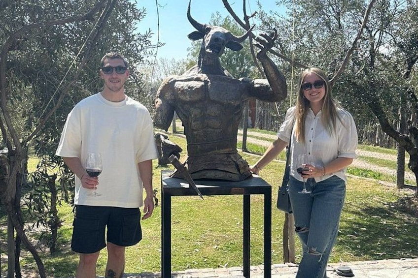 Two people standing next to a bronze bull sculpture in an outdoor setting with trees and grass. 4