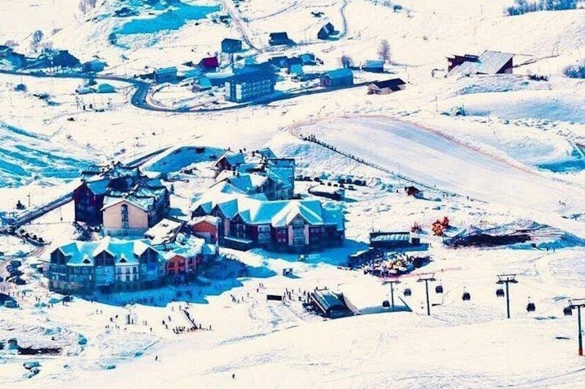 Un pueblo cubierto de nieve con edificios, un telesilla y un lago congelado. 1