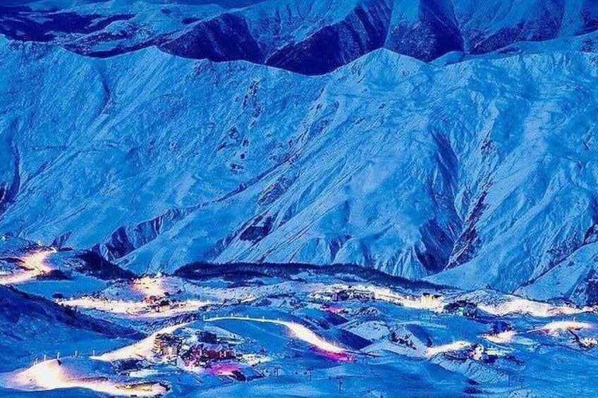 Un paisaje montañoso con picos nevados y un valle con luces dispersas. 5