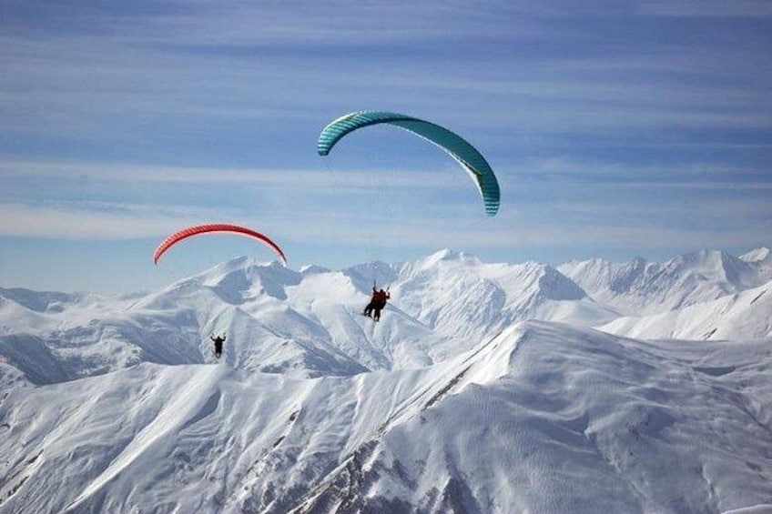 Dos parapentistas sobre un paisaje montañoso nevado. 2